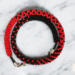 Red and black Crimson Noir Kumihimo necklace with tightly braided glass seed beads, photographed coiled on a marble surface